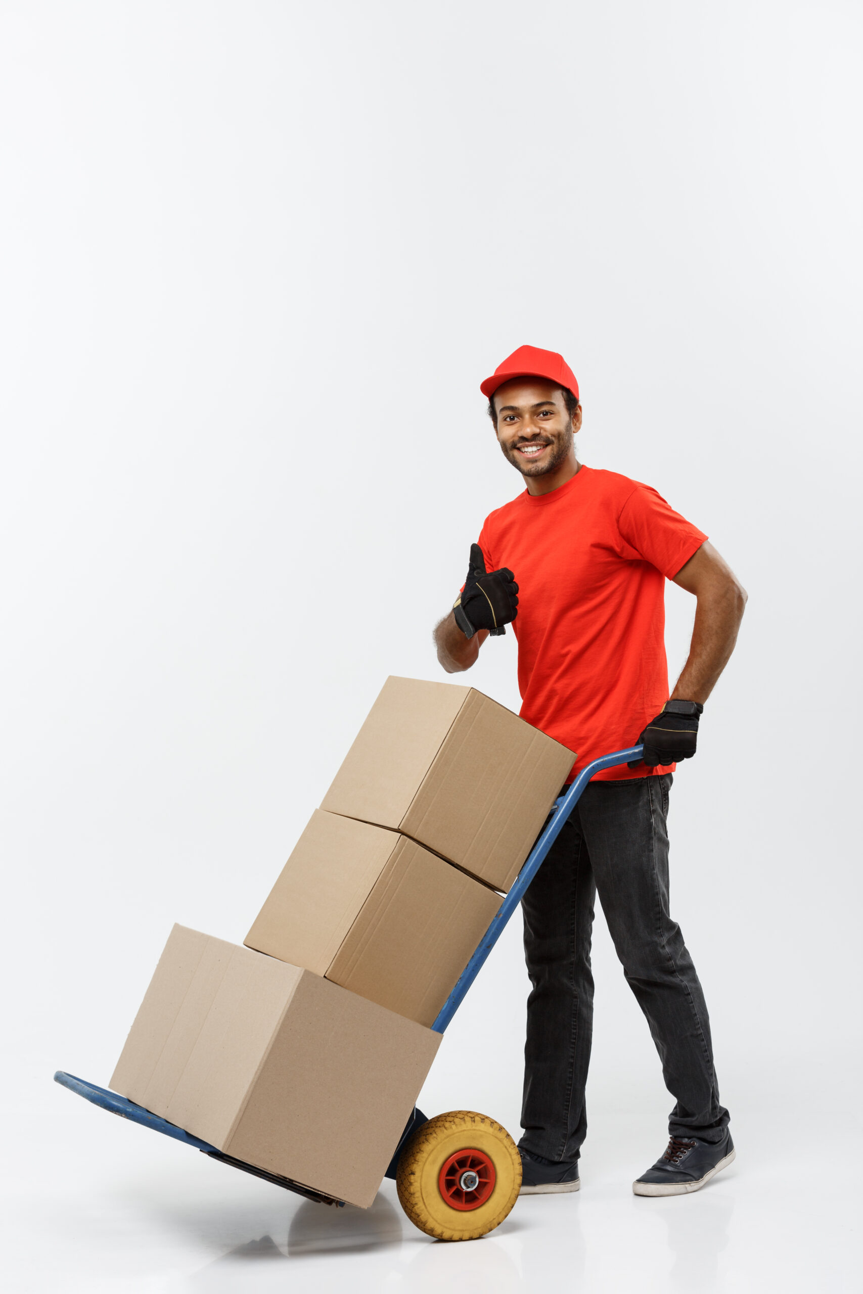 delivery concept portrait of handsome african american delivery man or courier pushing hand truck with stack of boxes. isolated on grey studio background. copy space.